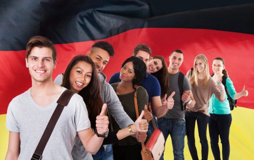 Group Of Multi Ethnic Students Standing In Front Of German Flag Showing Thumb Up